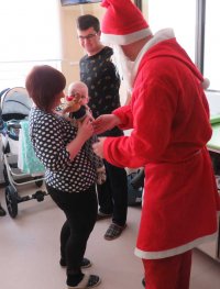 Mikołaj wręcza prezent małemu pacjentowi trzymanemu na rękach przez mamę
