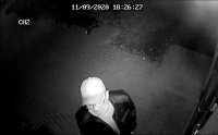 Fotografia z zapisu monitoringu, przedstawia sprawcę włamań do mieszkań w Bełchatowie. Mężczyzna ubrany na ciemno. Na głowie czarna czapka z daszkiem. Mężczyzna w okularach korekcyjnych, maseczka pod brodą