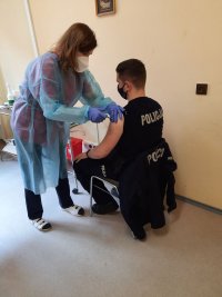 umundurowany policjant w punkcie szczepień . Lekarz podaje policjantowi szczepionkę