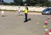 policjant z bełchatowskiej drogówki prowadzi egzaminy na kartę rowerową. Sprawdza umiejętności praktyczne ucznia który na rowerze pokonuje tor przeszkód