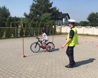 policjant z bełchatowskiej drogówki prowadzi egzaminy na kartę rowerową. Sprawdza umiejętności praktyczne ucznia który na rowerze pokonuje tor przeszkód