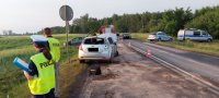 policjanci pracują  na miejscu wypadku drogowego w miejscowości Wadlew. Czołowo zderzyły się dwa auta. w tle widoczne uszkodzone pojazdy , jeden z nich marki Opel Vectra po dachowaniu. obok strażacy