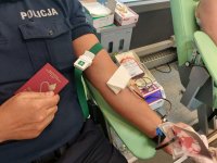 policjant oddaje krew. widoczny jest tylko fragment sylwetki policjanta, trzyma w ręku książeczkę krwiodawcy