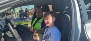policjant i dziecko, siedzą w samochodzie policyjnym , dziecko na siedzeniu kierowcy zdjęcie wykonane w czasie pikniku rodzinnego