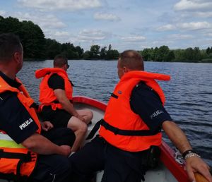 policjanci i ratownik na łódce na wodzie. patrolują teren zbiornika wodnego