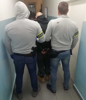 policjanci ubrani po cywilnemu  prowadzą osobę zatrzymaną. zdjęcie zrobione w na korytarzu