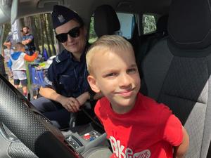 radiowóz policyjny, w którym siedzi chłopiec, który uśmiecha się, na siedzeniu pasażera siedzi policjantka