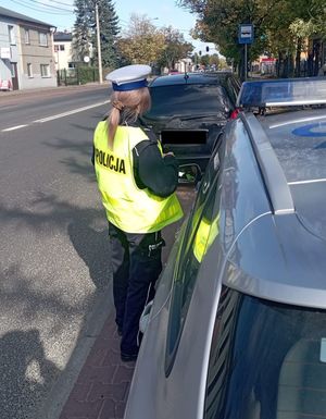 policjantka w trakcie kontroli pojazdu, kontroluje sprawność świateł pojazdu.