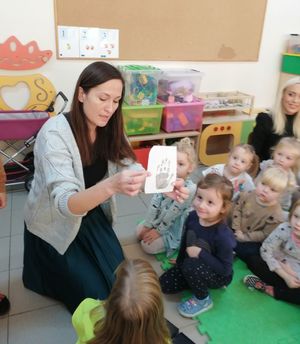 spotkanie z dziećmi, na zdjęciu dzieci w przedszkolu, pracownik z zespołu profilaktyki społecznej komendy który pokazuje dzieciom odbitkę dłoni na kartce.