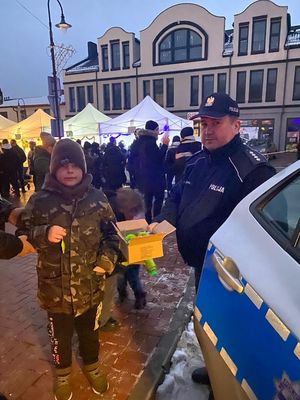 na świątecznym jarmarku policjantka rozdaje kamizelki odblaskowe. przy policjanci stoi kobieta która ma założoną kamizelkę odblaskową.