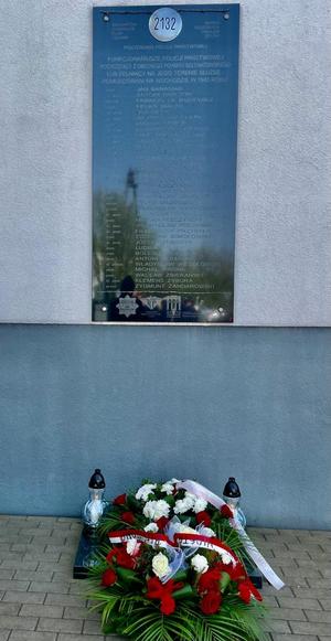 tablica upamiętniająca pomordowanych policjantów, pod tablicą kwiaty i znicze.