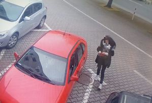 czerwony samochód osobowy na parkingu przy nim kobieta.