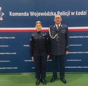 policjantka i policjant stoją na tle ścianki z napisem Komenda Wojewódzka Policji w Łodzi.