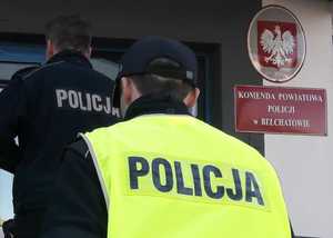 Dwóch policjantów wchodzi do budynku komendy, w tle widać tabliczkę z napisem Komenda Powiatowa Policji w Bełchatowie.