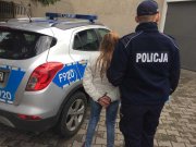 policjant prowadzi zatrzymaną kobietę podejrzewaną o kradzież alkoholu