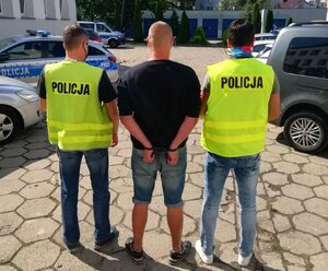 Funkcjonariusze w kamizelkach z napisem Policja prowadzą zatrzymanego