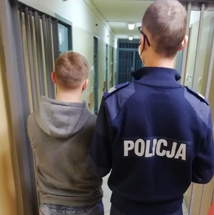 W pomieszczeniu komendy policji, umundurowany policjant prowadzi zatrzymanego.  Jest to osoba podejrzana do naruszenie nietykalności cielesnej mężczyzny.