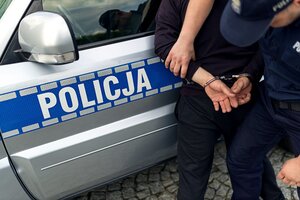 zdjęcie przedstawia fragment radiowozy z napisem na drzwiach policja oraz fragmenty sylwetek policjanta i osoby zatrzymanej