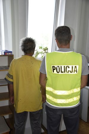 zdjęcie przedstawia policjanta wraz z zatrzymanym mężczyzną stojących tyłem