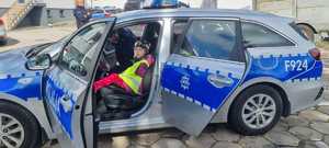 dziewczynka ubrana w kamizelkę odblaskową siedząca wewnątrz radiowozu policyjnego