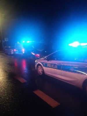 noc, miejsce zdarzenia drogowego, widoczny radiowóz policyjny i światła błyskowe, w tle samochód uczestniczący w zdarzeniu