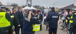 akcja rozdawania kamizelek odblaskowych na targowisku w Szczercowie. Policjanci i wójt gminy ubierają pieszych i rowerzystów w kamizelki