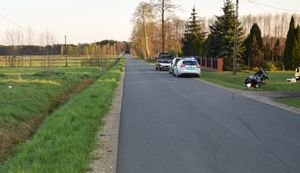 miejsce zdarzenia drogowego, droga w rowie przewrócony motocykl, obok radiowóz policyjny , w tle domostwa, pola i lasy