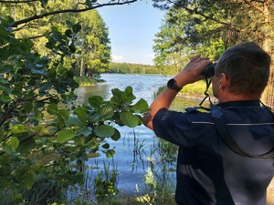 policjant nad zbiornikiem wodnym, patrzy przez lornetkę i kontroluje bezpieczeństwo nad wodą.