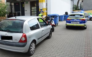 policjantka w trakcie oględzin pojazdów uczestniczących w zdarzeniu to jest samochodu marki renault i motoroweru. obok radiowozy policyjne. Miejsce na parkingu przed sklepem.