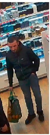 wygląd sprawcy kradzieży sklepowych, mężczyzna którego zarejestrowały kamery monitoringu w sklepie pomiędzy regałami.