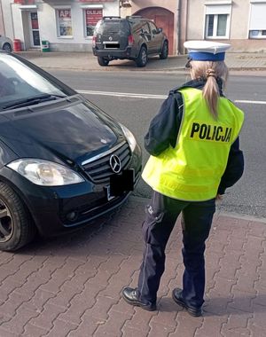 policjantka w trakcie kontroli pojazdu, kontroluje sprawność świateł pojazdu.
