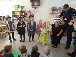spotkanie z policjantem, na zdjęciu dzieci w przedszkolu i policjant. dzieci przymierzają kask ochronny i mundur policyjny.