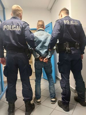 policjanci prowadzą zatrzymanego mężczyznę, zdjęcie zrobione na korytarzu komendy.