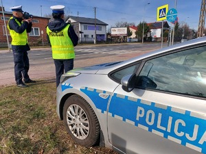 policjanci stoją przy radiowozie przy drodze i kontrolują prędkość pojazdów.