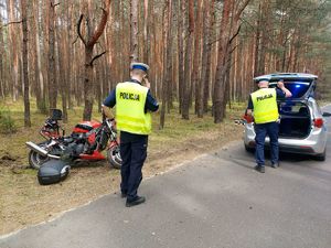 miejsce wypadku motocyklisty, droga, na poboczu przewrócony motocykl, na miejscu dwa pojazdy policyjne.policjanci wykonują oględziny miejsca zdarzenia.