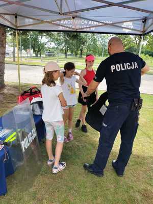 policjant i trójka dzieci, policjant pokazuje im wyposażenie policjanta do służby.