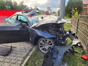 śmiertelny wypadek w miejscowości mierzynów. Na zdjęciu uszkodzony samochodu osobowego, który przodem wbił się w latarnię uliczną, dalej czerwony parawan, droga na której stoją pojazdy.