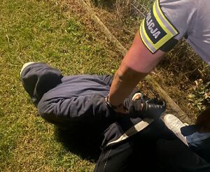 zatrzymany przez policjantów włamywacz leży na ziemi. Ma założone kajdanki na ręce trzymane z tyłu, na zdjęciu widać częściowo nieumundurowanego policjanta z opaską z napisem policja.