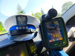 czapka policyjna, obok laserowy miernik prędkości, na jego wyświetlaczu widnieje wynik pomiaru prędkości.