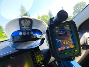 czapka policyjna, obok laserowy miernik prędkości, na jego wyświetlaczu widnieje wynik pomiaru prędkości.