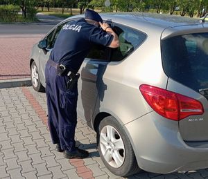 policjant zagląda przez okno do wnętrz zaparkowanego na parkingu pojazdu.