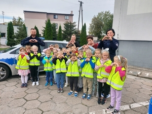 policjanci w czasie spotkania z przedszkolakami na dziedzińcu komendy Policji. dzieci ubrane w kamizelki odblaskowe.