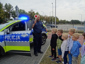 dzielnicowi na spotkaniu z dziećmi. w tle radiowóz.