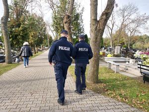 dwóch umundurowanych policjantów patroluje teren cmentarza.