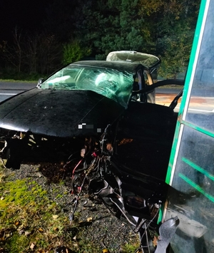 uszkodzony samochód który uszkodzony stoi w poprzek drogi przy przystanku autobusowym.