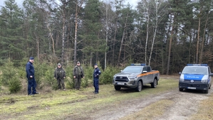 Na zdjęciu funkcjonariusze Policji ze Strażą Leśną na tle radiowozów.