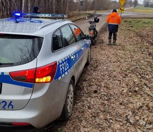 na zdjęciu radiowóz policyjny, który stoi na drodze obok motocykl i mężczyzna.