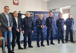 w pomieszczeniu służbowym stoją umundurowani i nieumundurowani policjanci.