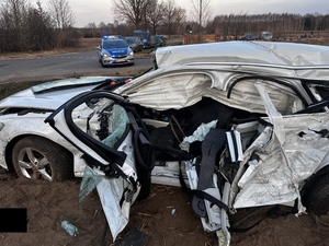 miejsce wypadku drogowego, przy skrzyżowaniu ulic, rozbity samochód osobowy stoi na poboczu drogi, dalej widać radiowóz policyjny.