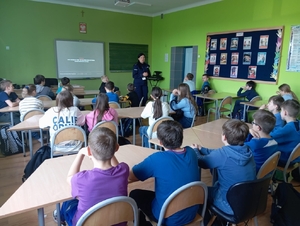 policjantka w czasie spotkania z dziećmi w szkole. Uczniowie siedzą w ławkach a policjantka prowadzi prelekcję na temat bezpieczeństwa.